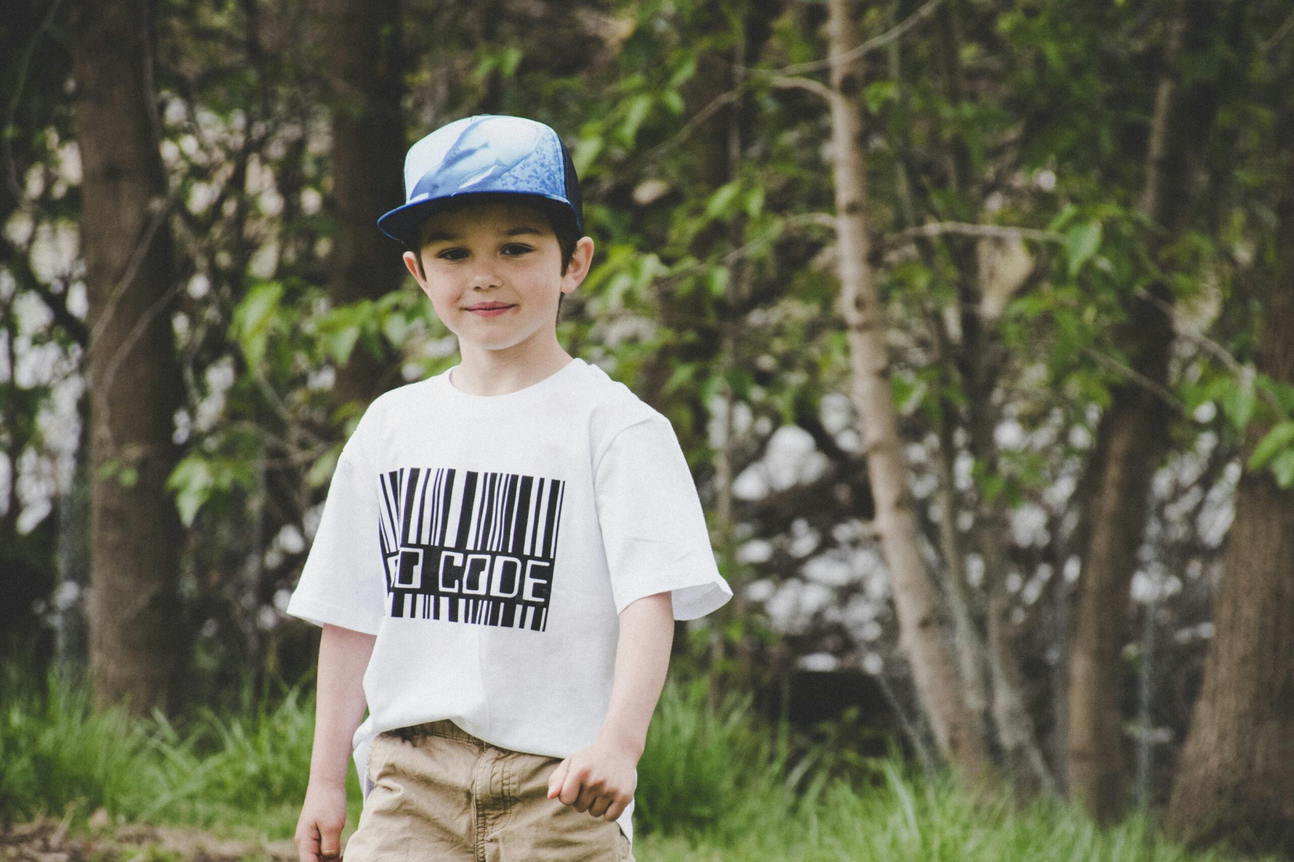 A cheerful young boy wearing a stylish t-shirt and cap, enjoying the outdoors.