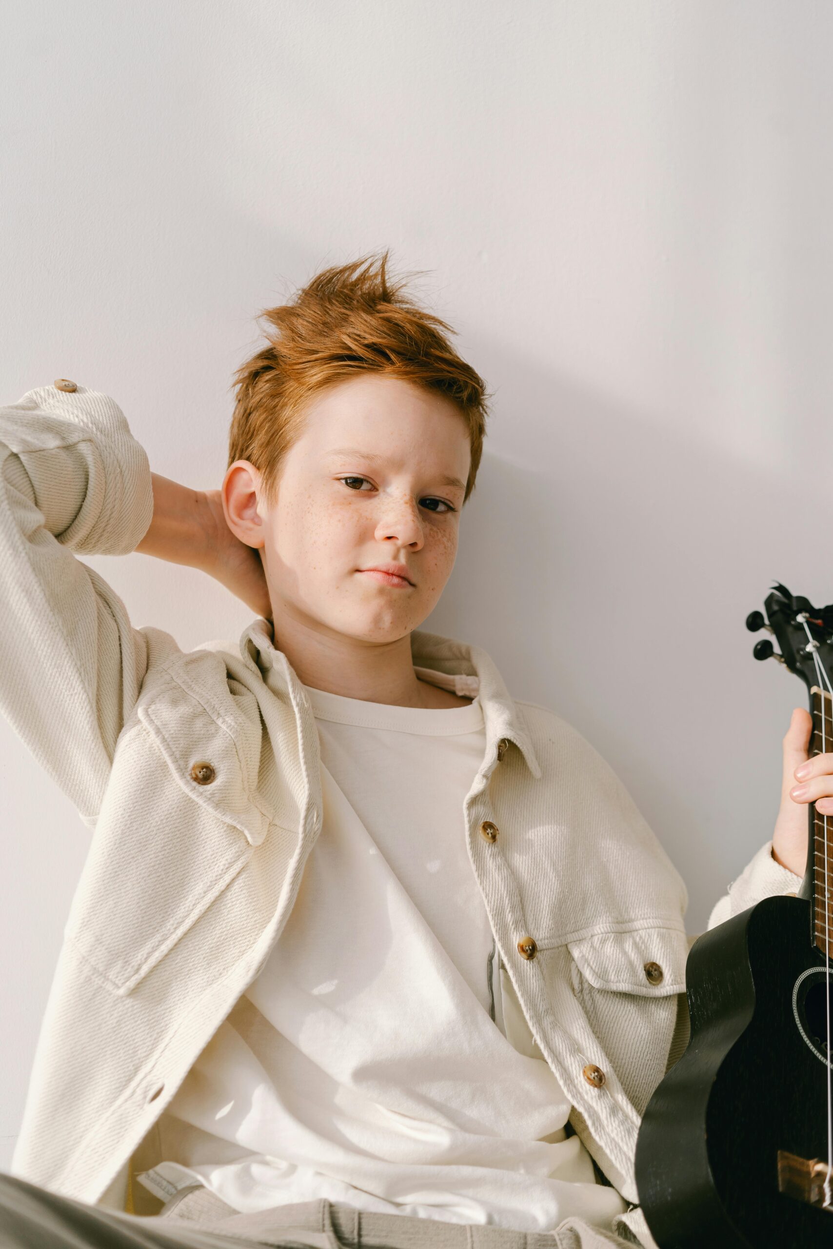 Teen boy holding a ukulele indoors, dressed in a casual jacket, embodying youthful charm.